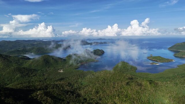 Horizontal panning aerial shot above Linapacan Island featuring low altitude clouds drifting over coastal terrain and calm blue ocean waters, Philippines