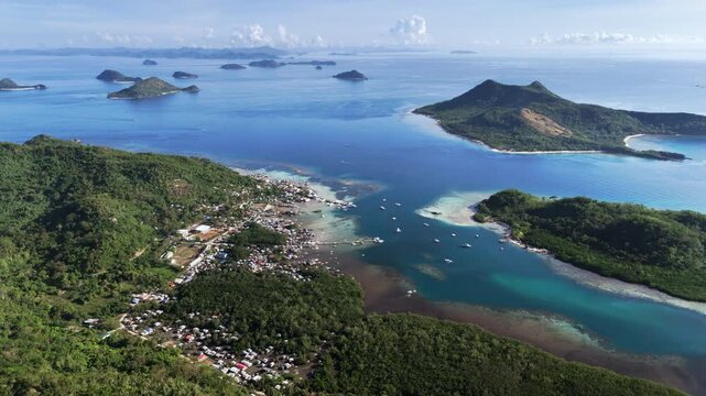 High-altitude aerial horizontal panning shot over Linapacan Island, Palawan, revealing a peaceful coastal community surrounded by calm turquoise waters in the morning light, Philippines