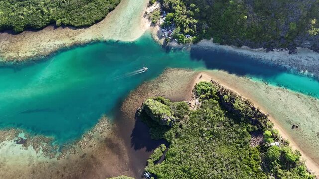 High-altitude overhead tracking shot of an outrigger boat crossing a narrow crystal-clear channel between islands in Linapacan, Palawan, during a calm morning, Philippines
