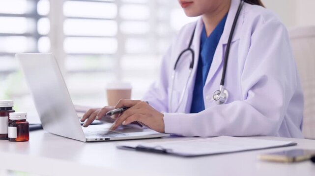 Asian adult female doctor professional using laptop computer for patient care medical records online consultation at clinic office modern healthcare setting
