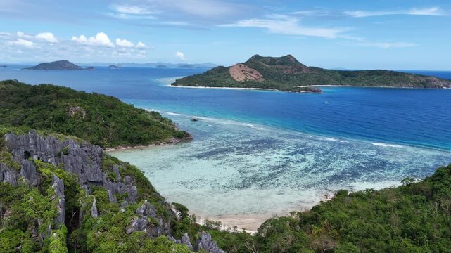 Horizontal panning aerial shot over Ile Island showcasing limestone cliffs, shallow and deep water contrast, and distant views of Patoyo Island, Philippines
