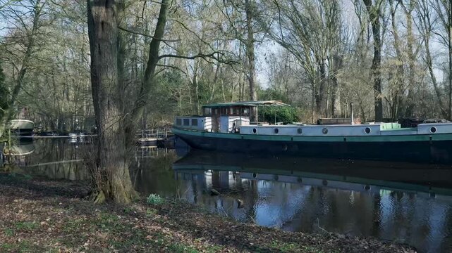 Barge moored on calm canal water in a leafless forest