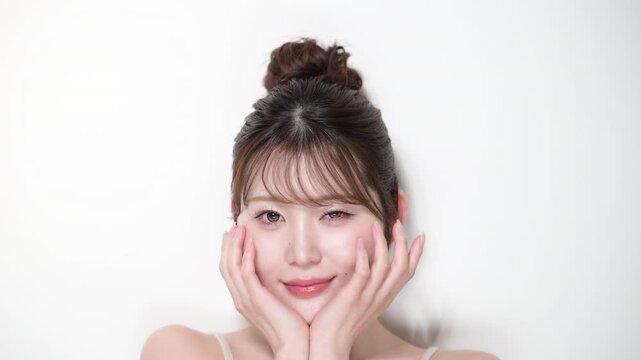 お団子のアップヘアの若い女性の艶や透明感やツヤ肌のビューティー　カメラ目線でウィンク　エステやカラコンやまつ毛パーマなどのかわいいイメージの動画　スローモーション