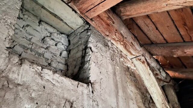 Rough whitewashed brick wall with cracks beneath aged wooden beams and planks, dim lighting highlighting worn textures and rustic atmosphere of an old building