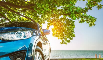 Blue sport SUV car parked by the tropical sea under umbrella tree. Summer vacation at the beach. Summer travel by car. Road trip. Automotive industry. Hybrid and electric car concept. Summer vibes. © Fahroni