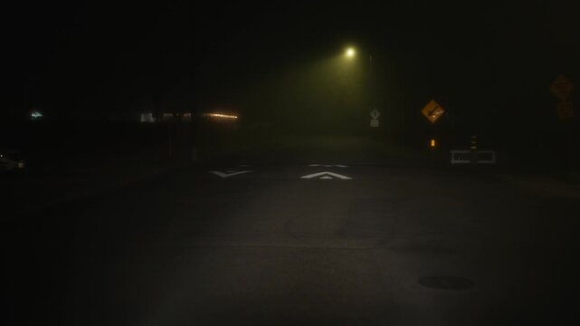 Driving through foggy night street with arrow marking, forward motion along the road in dense fog creates quiet atmosphere of low visibility and empty residential area