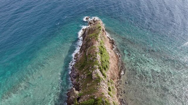 Overhead riser drone shot of a rocky cape at Ile Island surrounded by turquoise waters and gentle waves washing the shoreline, Philippines
