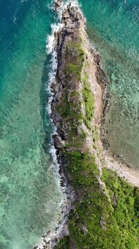 Portrait overhead push-in reveal shot of a rocky cape at Ile Island with crystal clear waters and soft waves surrounding the shoreline, Philippines
