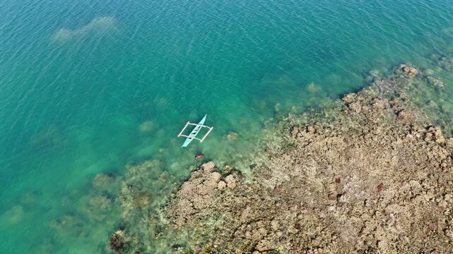 POI orbit drone shot of a fisherman swimming beside his small outrigger boat fishing in the reef at Linapacan, Palawan, Philippines
