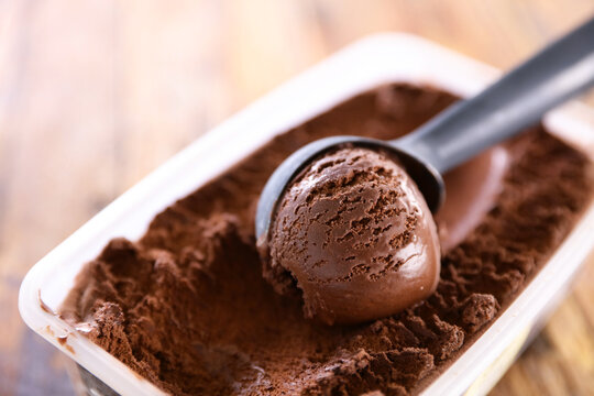 Scoop of dark chocolate ice cream in container with professional scooper