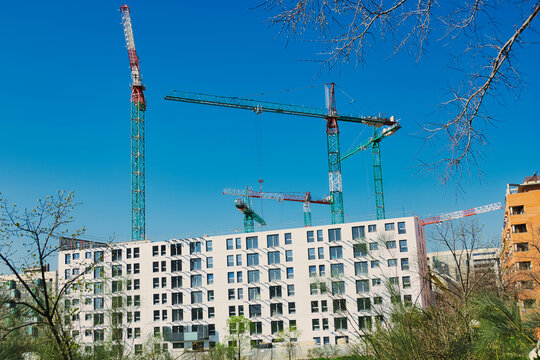 Multiple tower cranes at a construction site for new residential apartments under a clear blue sky, representing urban development, real estate investment, and the rising cost of housing.