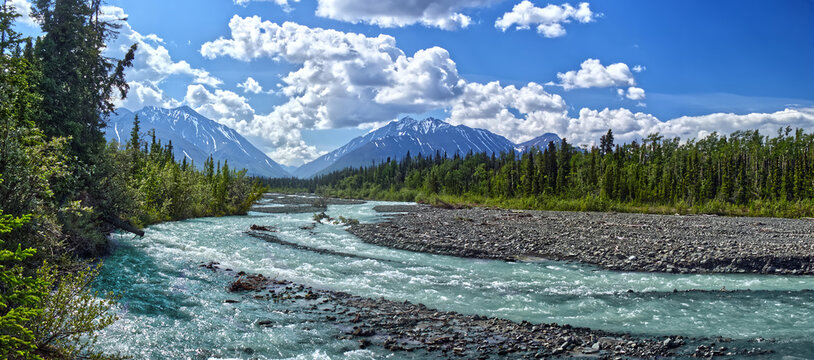 Panoramic view of the teal rapids of the Kathleen river on a bright summer afternoon. Distant clouds over the forests and the mountains adds to the beauty. Kluane National Park. YT, Canada
