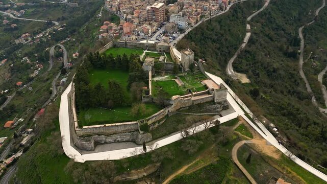 Aerial view of Lombard castle in Enna, showcasing the expansive green grounds, stone walls, and surrounding urban landscape with winding roads and buildings