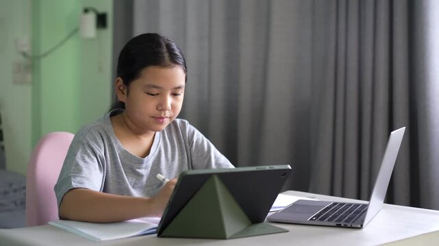 asian child student write learning on computer tablet screen or kid girl fun studying writing by video call talking on study online class by laptop notebook or young people learn from home school