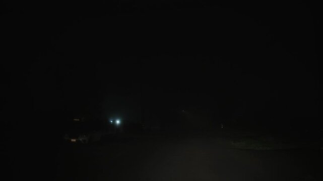 Driving along dark night street in dense fog, forward camera movement on an almost completely obscured road, faint diffused streetlight glow barely visible through thick haze