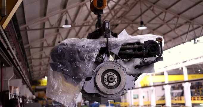 Industrial crane meticulously lifting a large diesel engine on an assembly line inside a modern vehicle manufacturing factory. Heavy machinery production and advanced industrial automation concept
