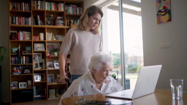 Daughter helping elderly mother use laptop and online banking.