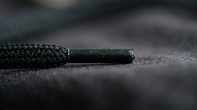 Close-up of a black shoelace aglet on a dark surface.