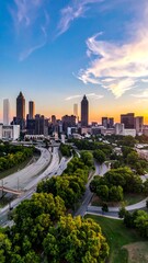 Fototapeta premium An aerial view showcases a cityscape with high-rise buildings silhouetted against a vibrant sunset sky with puffy clouds. Lush green trees are below
