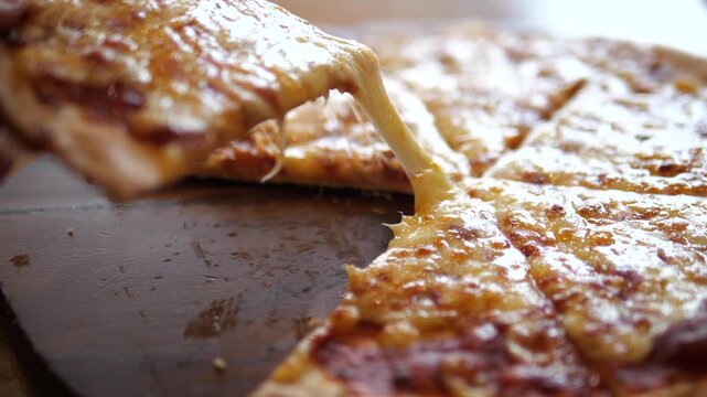 Close-up of hand lifting a slice of thin crust pizza with hot melting cheese pull on wooden board for restaurant advertisement