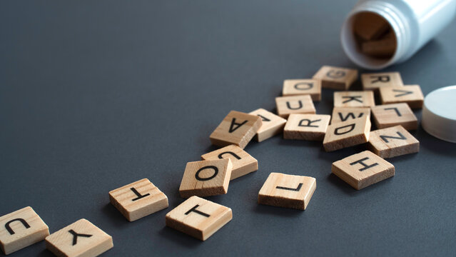 Wooden alphabet tiles spilling out of a white medical pill bottle on a dark grey background representing health literacy and medical terminology