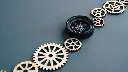 Black magnetic compass placed on a path of wooden gears symbolizing business direction and finding the right path in industry. © MohamadFaizal