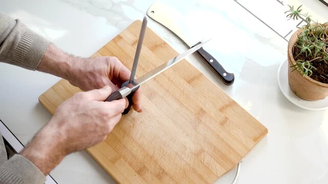 Sharpening a kitchen knife with a honing rod on wooden cutting board. Knife maintenance and culinary precision concept. Ideal for cooking and kitchen tool content. Clean, organized workspace. Daylight