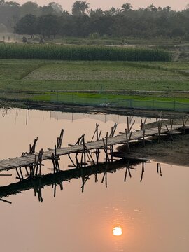 A serene rural landscape with a wooden bridge over a pond at sunset with trees and fields in the background shot on iphone photography
