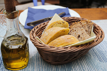 Basket with fresh bread slices served on table with olive oil bottle. Rustic food setting in...