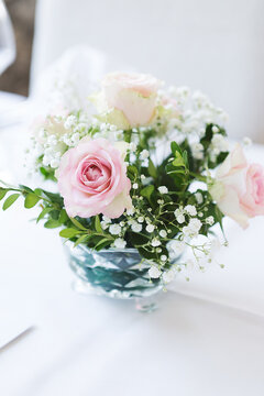 Elegant floral centerpiece with soft pink roses and white baby's breath in a crystal bowl on a white tablecloth. Perfect for wedding decor, romantic celebrations, and sophisticated event styling.