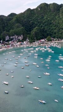 Aerial drone view of traditional banca boats anchored in the turquoise waters of Bacuit Bay near El Nido, Palawan, Philippines. Vertical