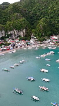 Aerial drone view of a small coastal village connected by a narrow sandbar and surrounded by shallow turquoise waters in El Nido, Palawan. Vertical