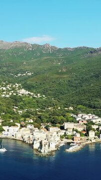 Scenic aerial shot of the picturesque coastal village of Erbalunga, nestled between lush green hills and the blue Mediterranean Sea in Corsica.