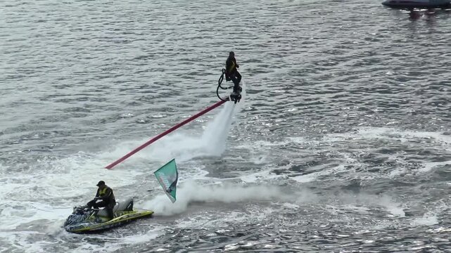 Murmansk, RUSSIA - June 29, 2013. International festival of Murmansk mile. Athlete on the flyboard floats and dives in the dark blue water with scenic sun highlights. Next to the boat with the compres
