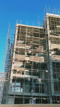 Under-construction high-rise residential building featuring concrete block structure. Exterior top levels view showcasing modern architectural design against clear blue sky. Multi-story apartment site