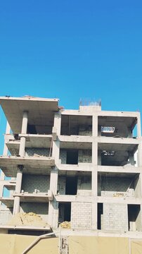 Under-construction high-rise residential building featuring concrete block structure. Exterior top levels view showcasing modern architectural design against clear blue sky. Multi-story apartment site