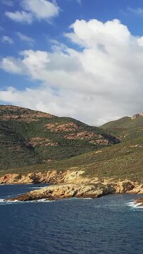 Scenic view of the rugged coastline and hills at Delta du Fango in Corsica, with clear blue water and dramatic clouds overhead.