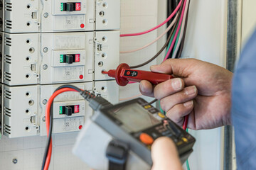 分電盤のブレーカー回路をテスターで精密点検する電気工事士の手元 © Buppy