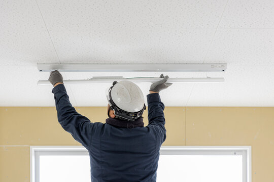 天井にLEDベースライト照明を設置する電気工事士の後ろ姿