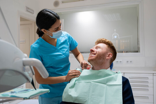 Dental professional placing a bib on a happy patient in a clinic