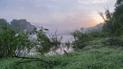 A tranquil morning scene of a misty river at sunrise, surrounded by lush green vegetation © Александр Арендарь