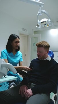 Female dental assistant shows information on a tablet to a male patient sitting in a dental chair