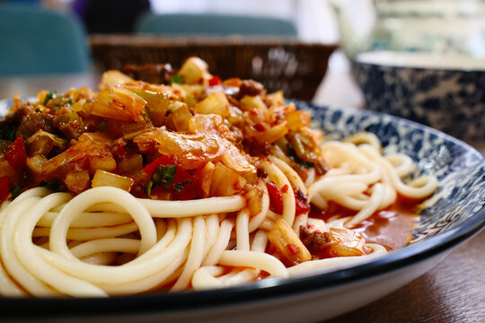 Traditional Uyghur suiru lagman noodles with meat tomato vegetable sauce served in blue ornate bowl closeup