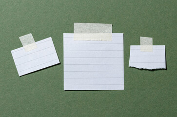 Blank ruled white paper memo notes or reminders with lines and copy space for text with adhesive sticky tape on green background flat lay top view