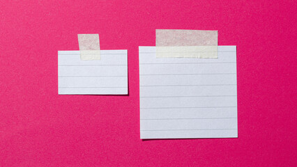 Blank ruled white paper memo notes or reminders with lines and copy space for text with adhesive sticky tape on pink background flat lay top view