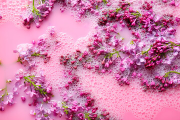 Obraz premium Lilac flowers in pink liquid with soap bubbles, closeup