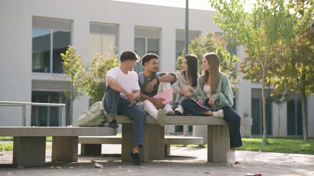 group of young friends sitting on a bench in the college courtyard. University classmates working together on an assignment