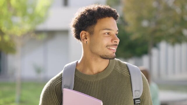 Handsome young male student with a backpack and notebook smiling at the camera. Portrait of a happy guy standing outdoors on a university campus