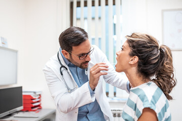 Professional male doctor examining a young woman's throat with a tongue depressor in a medical...