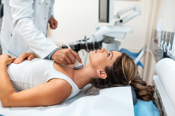 Obraz na płótnie Canvas Doctor performing a thyroid ultrasound scan on a female patient lying on an exam table in a clinic. Medical professional using a transducer probe for diagnostic imaging of the neck and glands.